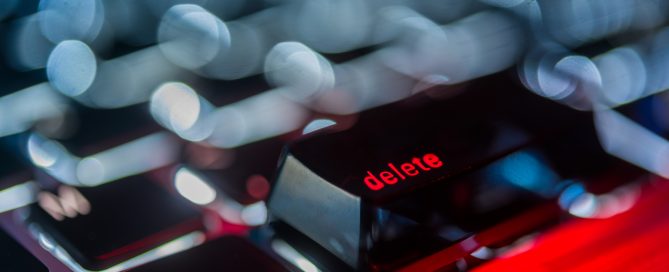 a computer keyboard with the delete key highlighted, the word delete is red